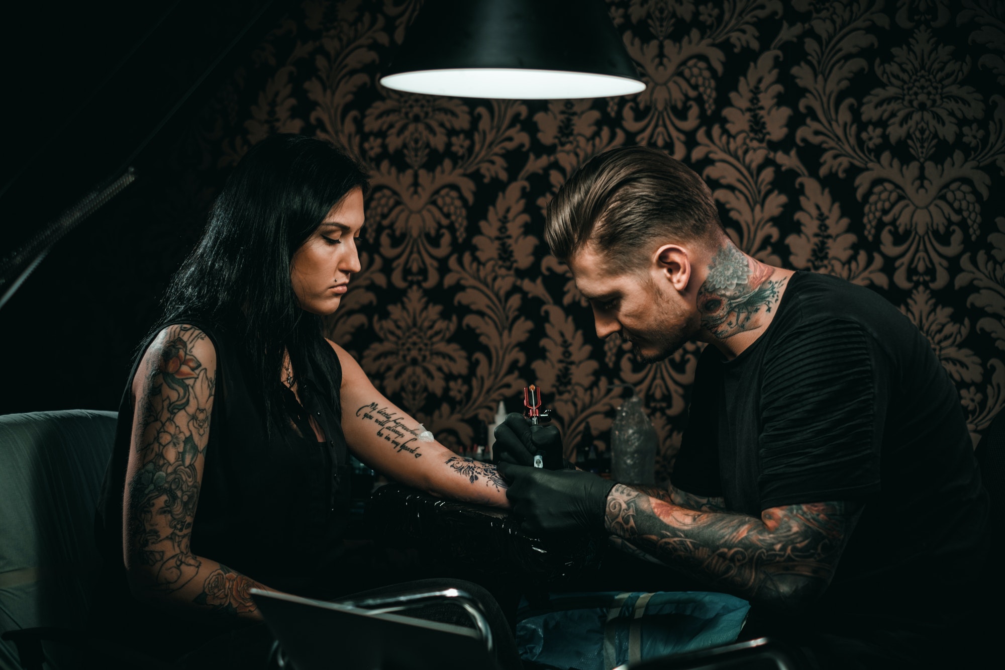 Tattoo artist inking detailed script on client's arm